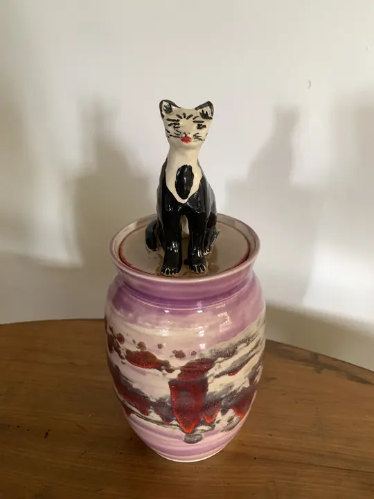 Pot mauve et rouge au couvercle surmonté d'un chat noir et blanc